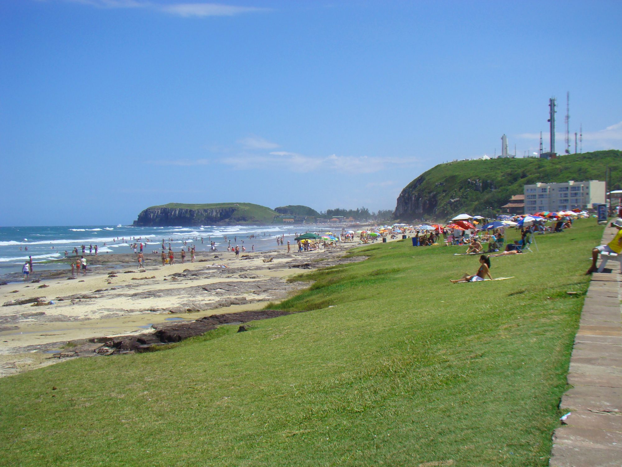 Um trecho central e acolhedor, entre gramados, rochas e vista para o Morro do Farol.
