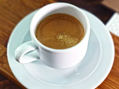 Xícara branca com café sobre um pires e uma mesa de madeira. Foto ilustrativa de Shameel Mukkath, Pexels.