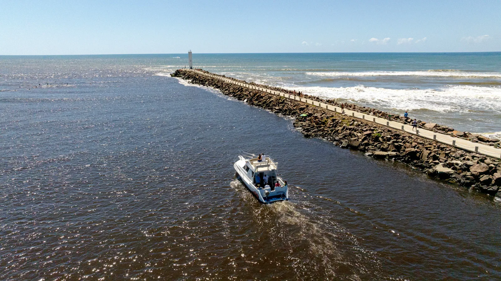 Vista aérea de um barco junto ao caminho de pedras e ao farol dos Molhes da Barra