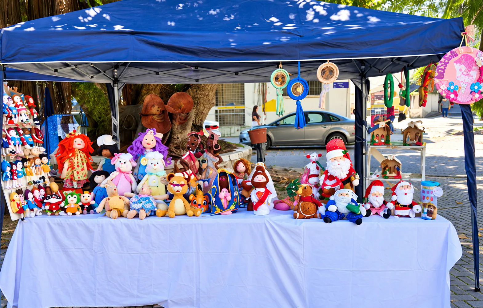 Mesa com bonecos de tecido e crochê, animais e peças natalinas sob uma tenda azul.