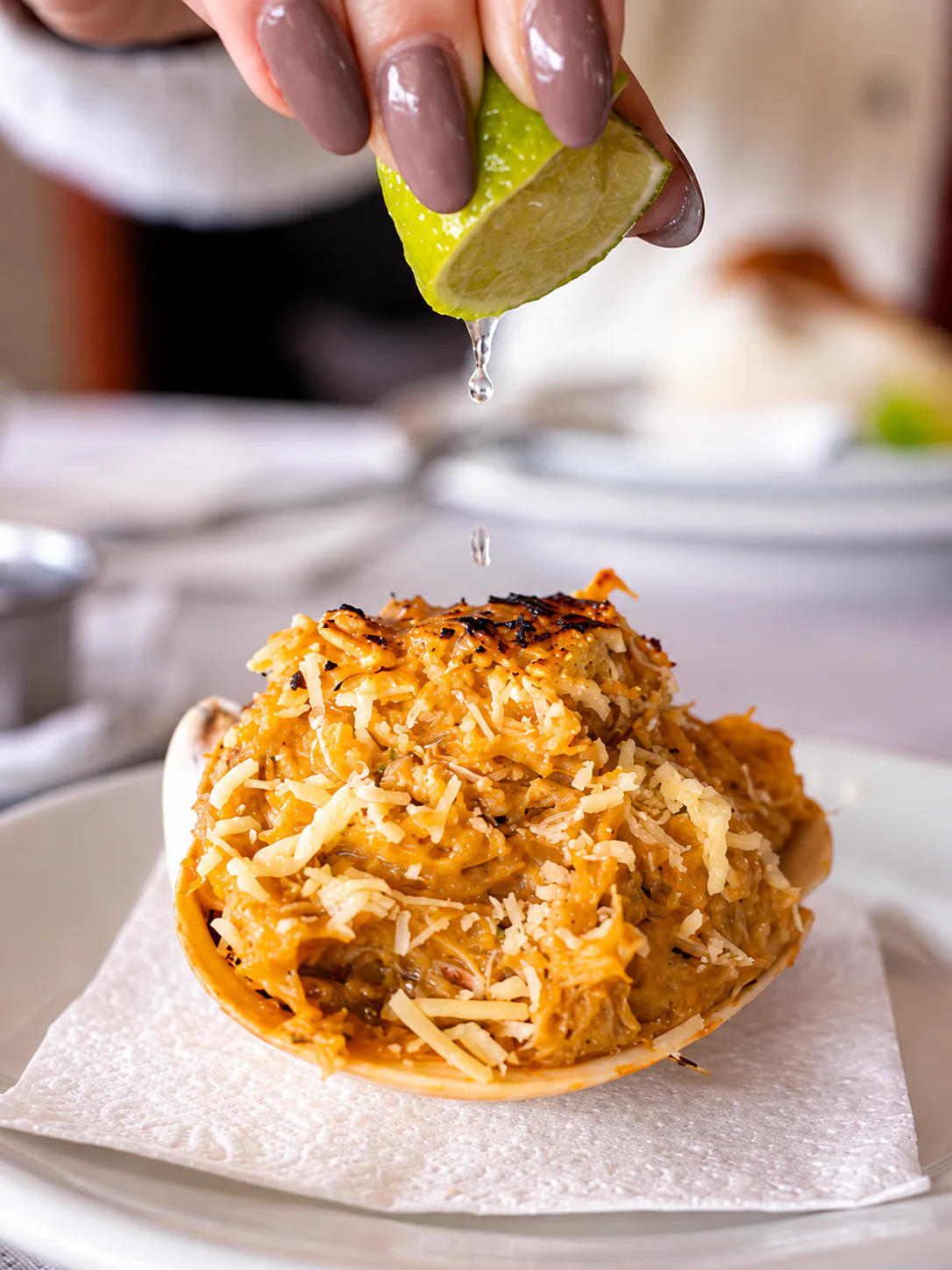 Casquinha gratinada recebendo limão espremido