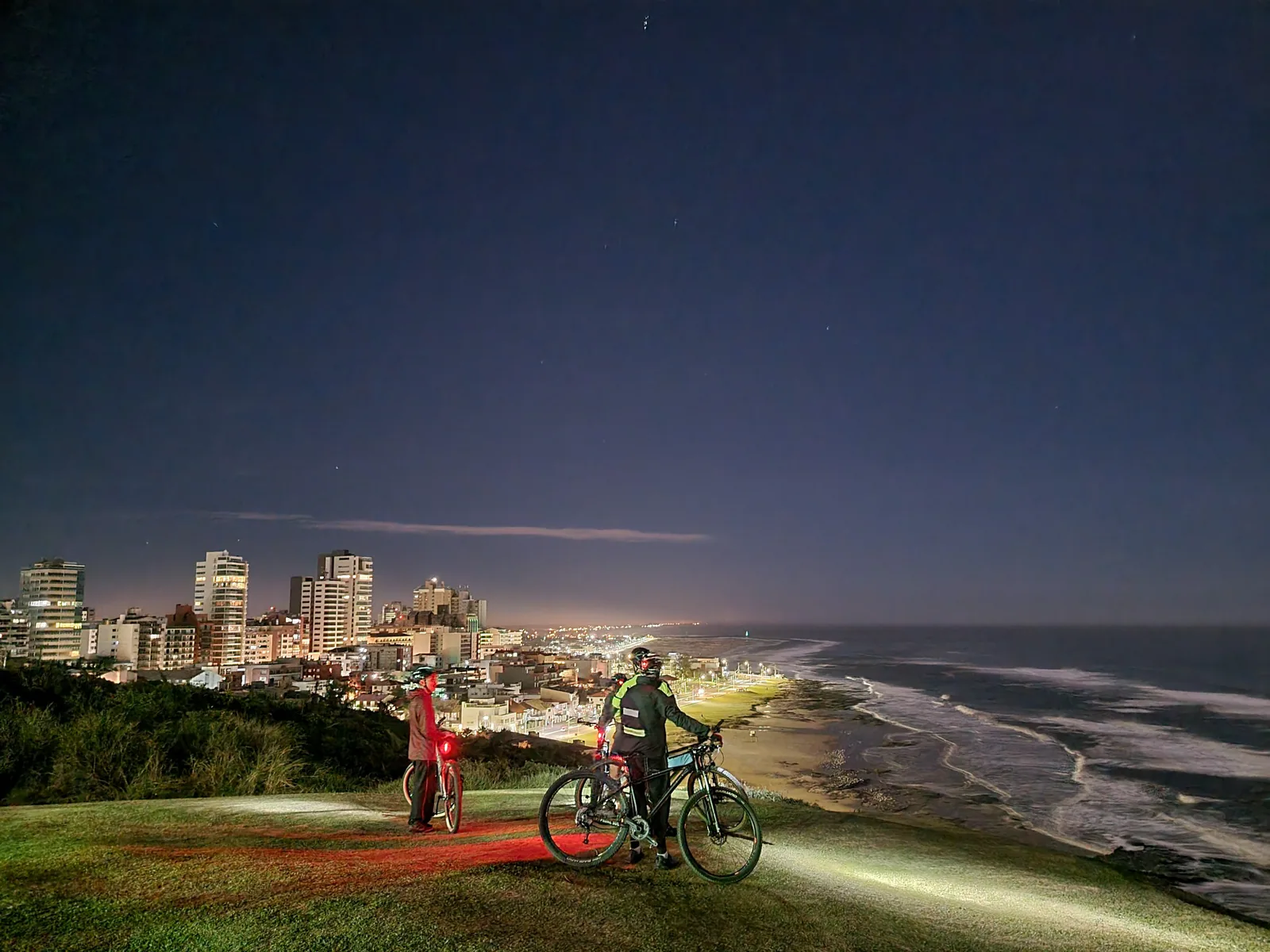 Ciclistas en el Morro do Farol de noche, frente a la costa iluminada
