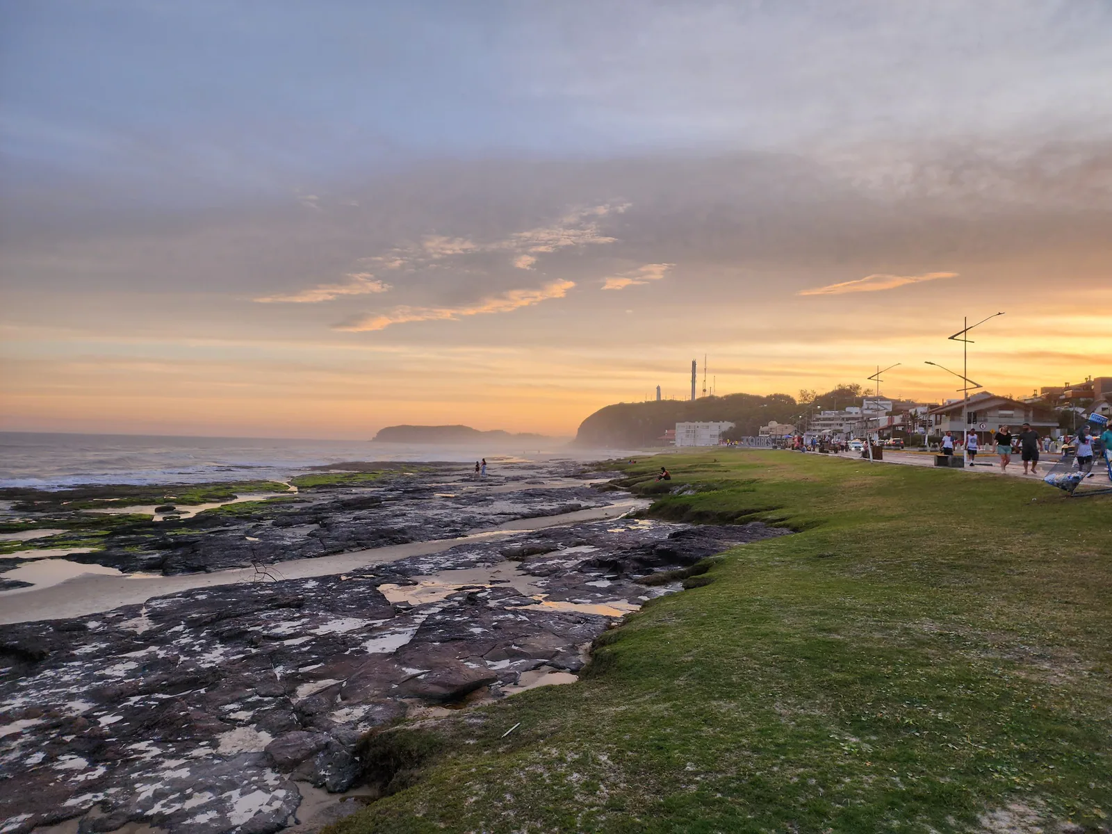 Rocas y césped de Prainha al atardecer, con el Morro do Farol al fondo
