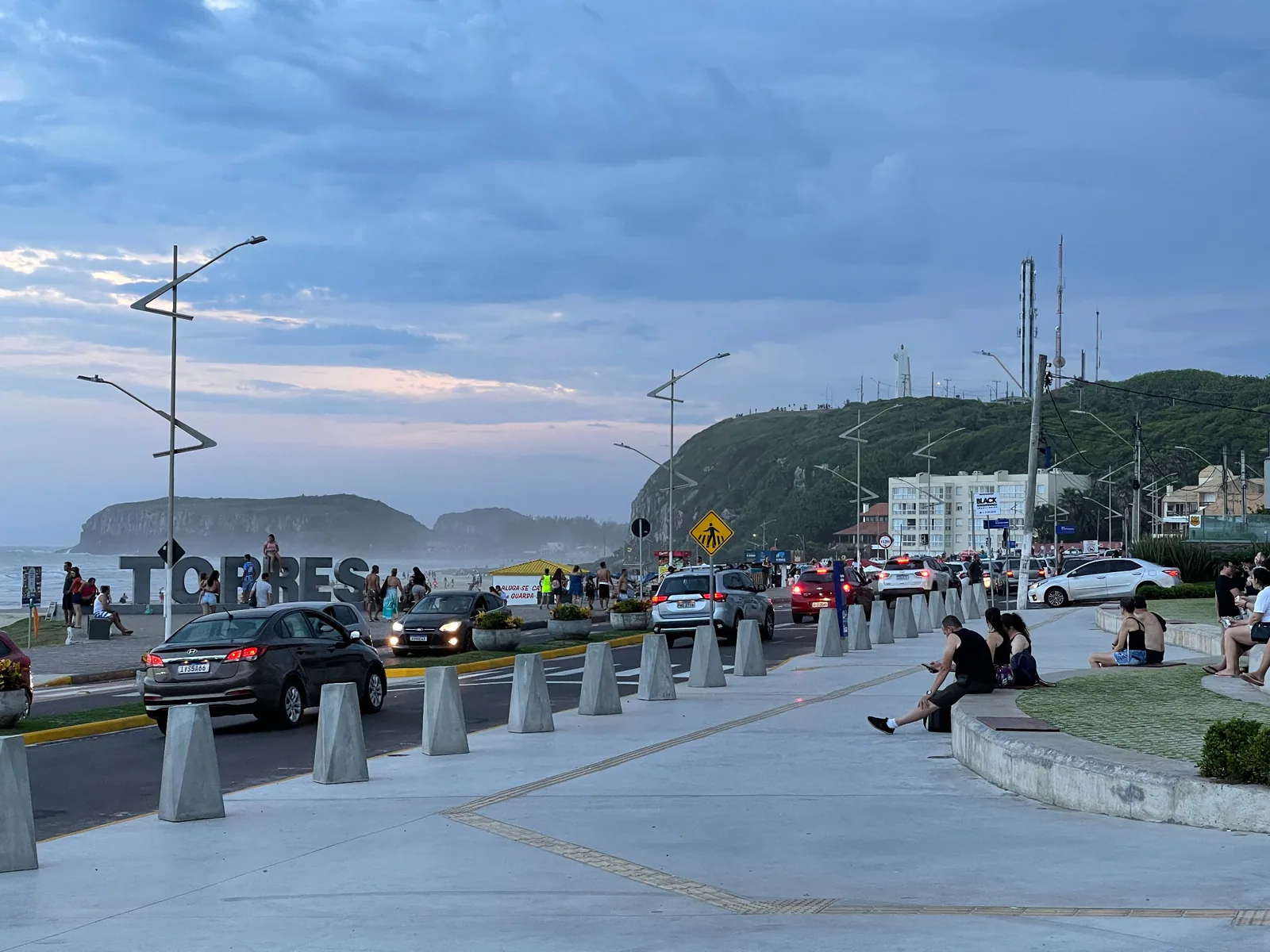 Personas paseando por la costanera de Prainha, con el letrero Torres al fondo