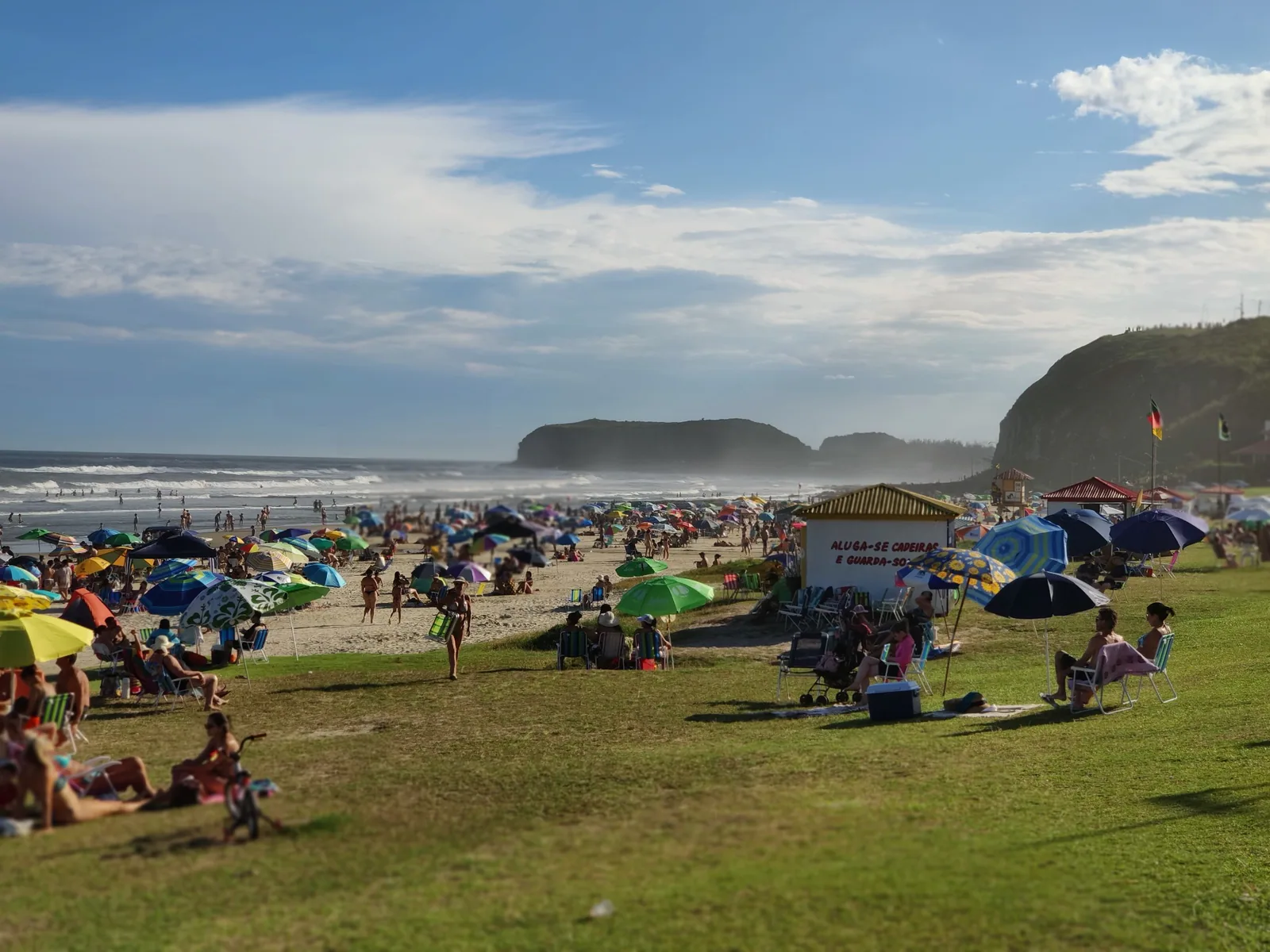 Prainha con bañistas y sombrillas, entre el césped y el Morro do Farol