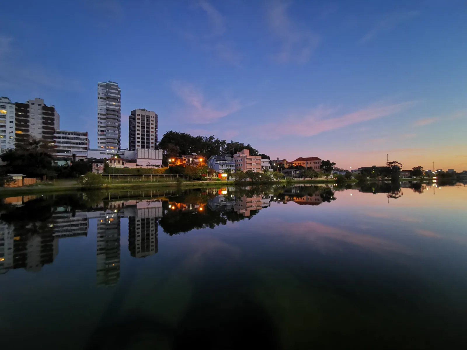 Building lights reflected on Lagoa do Violão beneath a pink evening sky
