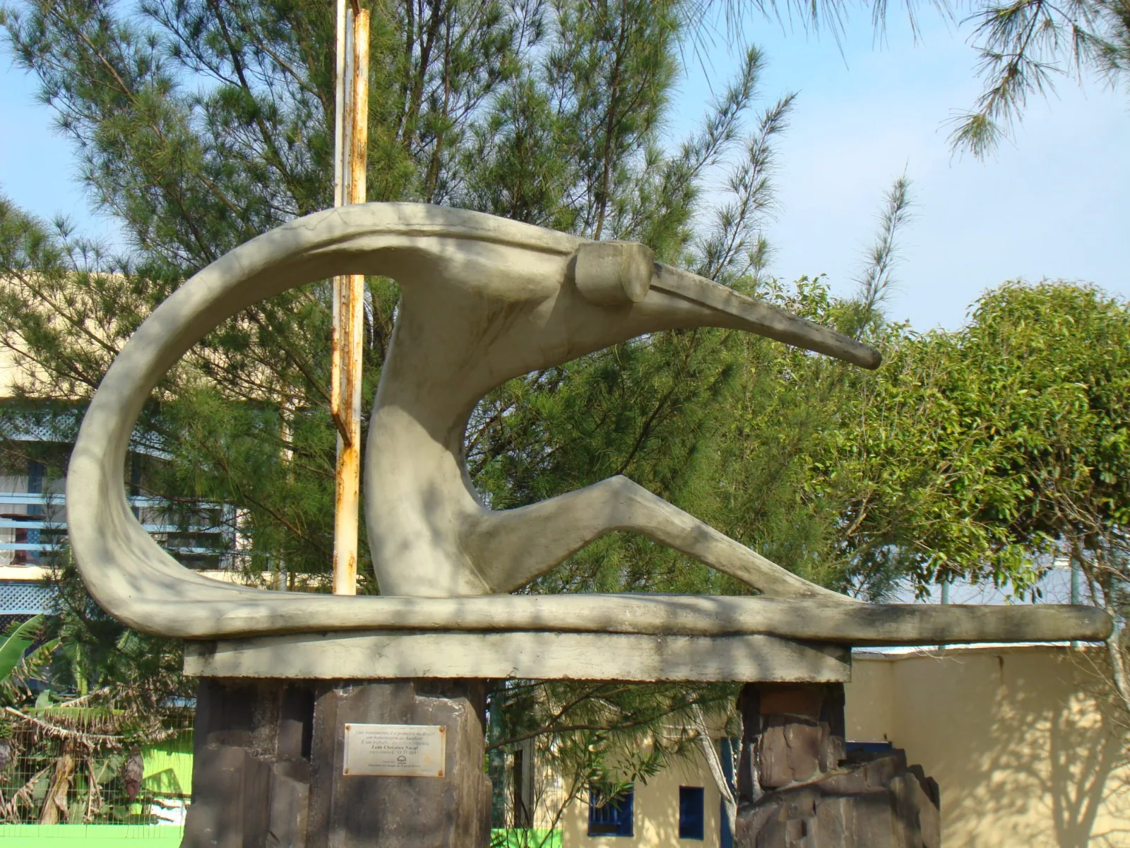 Escultura O Tubo, com vegetação e construções do entorno ao fundo